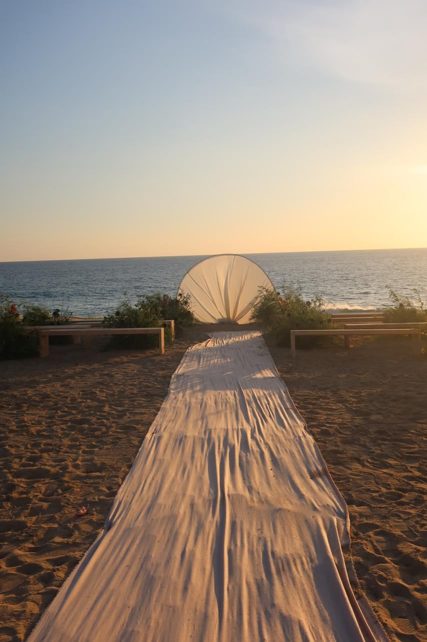 Beach ceremony aisle leading to a fan-shaped arch at the water