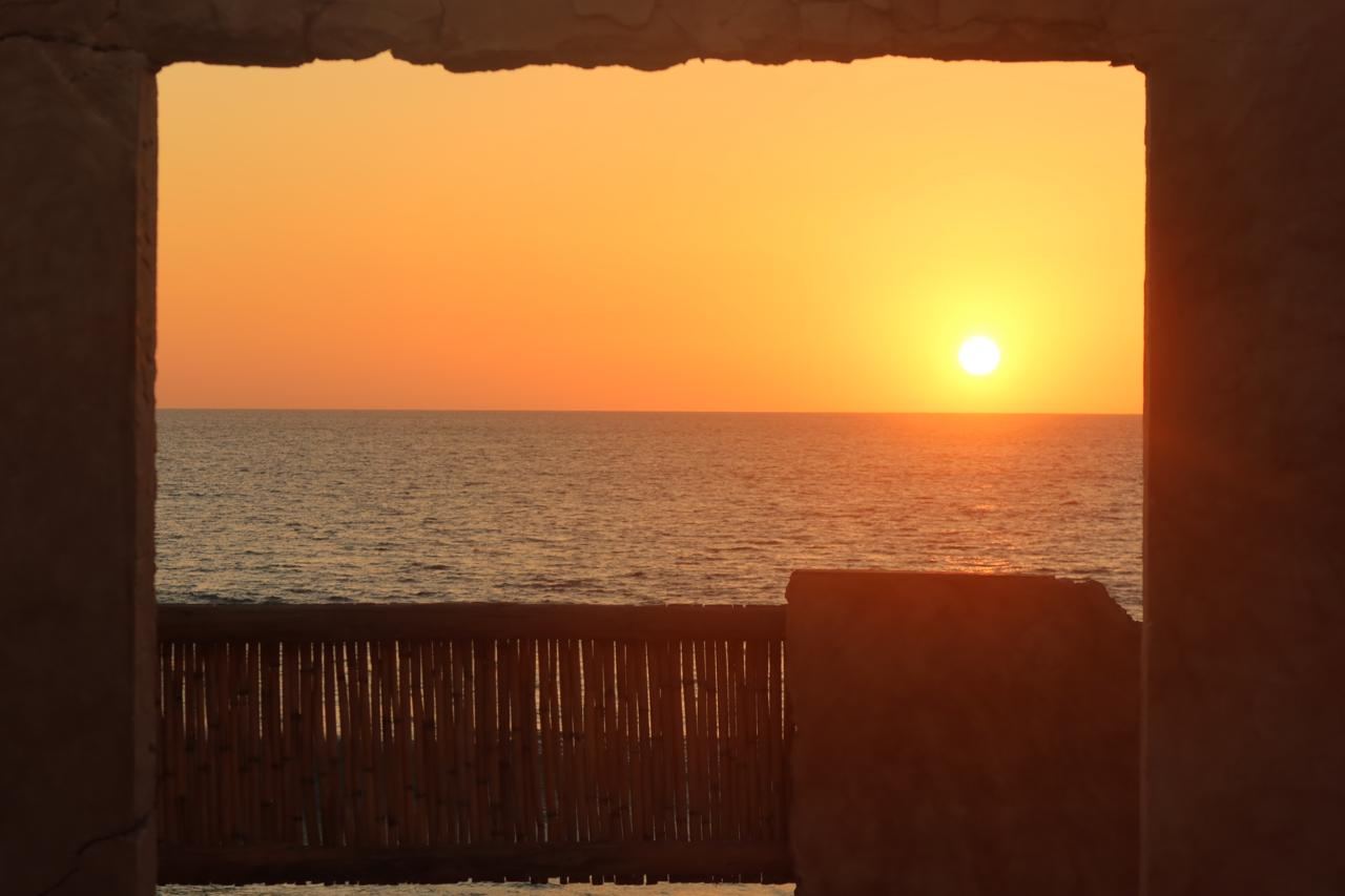 The sun setting over the sea, framed by a stone window
